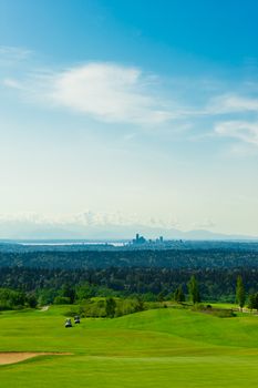 An aerial view from the top of the hill in a green golf course with Seattle downtown at the background.