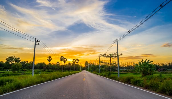 asphalt road through the green field on twilight sunset.