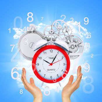 Hands hold alarm clock with figures and gears. Blue background