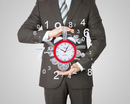 Businessman hold alarm clock with springs and gears. Gray background