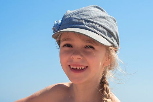 Adorable happy little girl in denim cap on the beach