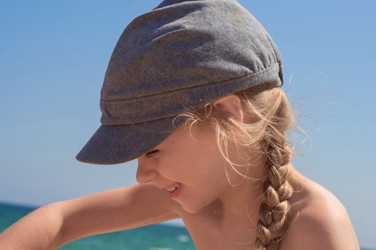 Adorable little girl in denim cap on the beach