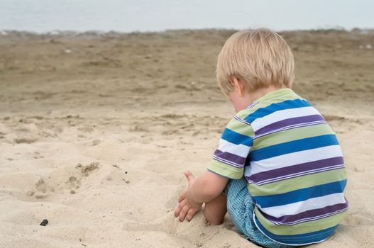 Little toddler boy in striped t-shirt sitting back on sandy beach