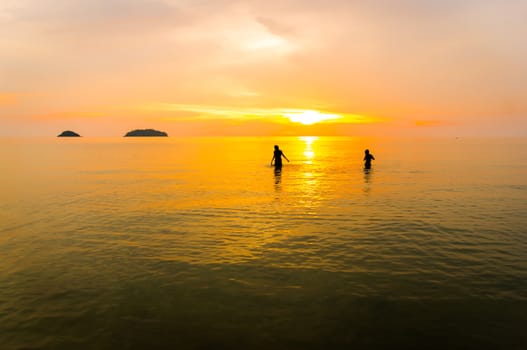 Silhouettes two man in ocean at sunset