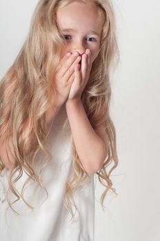 Little girl in white dress covers her mouth with her palms