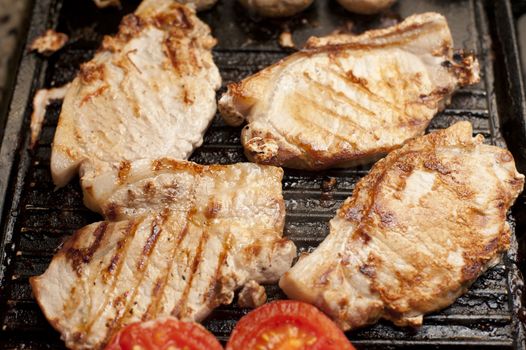Grilled pork chops and tomatoes on a griddle ready to be served for a tasty luch or dinner, high angle view