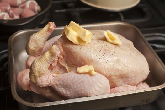Uncooked seasoned turkey topped with dollops of butter in a roasting pan or oven dish waiting to be placed in the oven for roasting