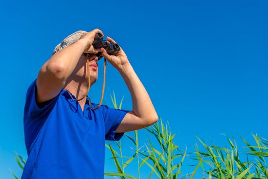 man with binoculars examines bird in the sky