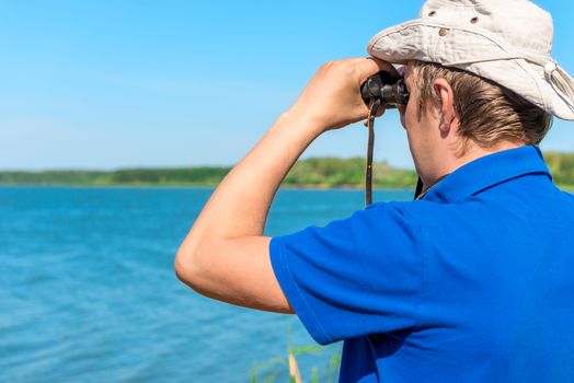 man with binoculars looks for something on the lake