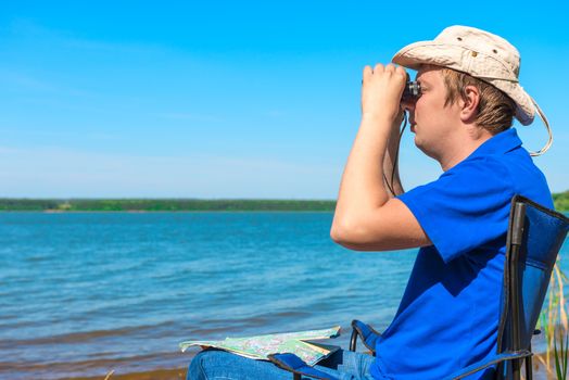 young man near the lake looking through binoculars
