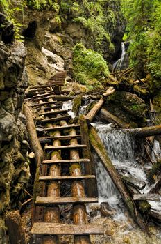 Close-up view of a trail made of wooden ladders with a waterfall nearby, Slovak Paradise National Park