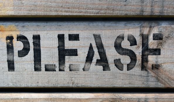 The word PLEASE stencilled in block capitals with black paint on wood