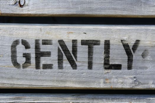 The word GENTLY stencilled in block capitals with black paint on wood