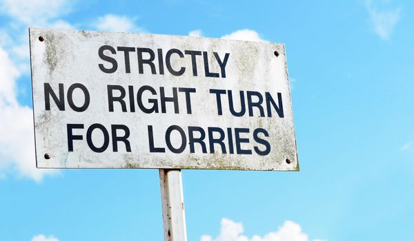 Weathered traffic warning sign against a blue sky advises that there is strictly no right turn for lorries