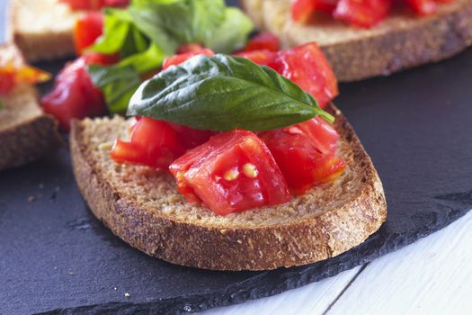 Bruschetta with tomato and basil over black stone plate, close up