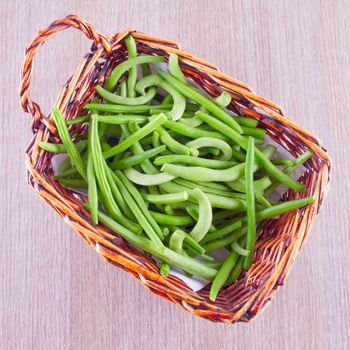 Grean beans in a small basket, over wooden table