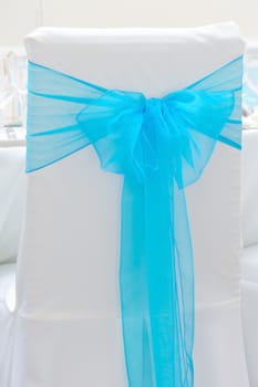White chair with blue ribbon tied in a bow at wedding reception