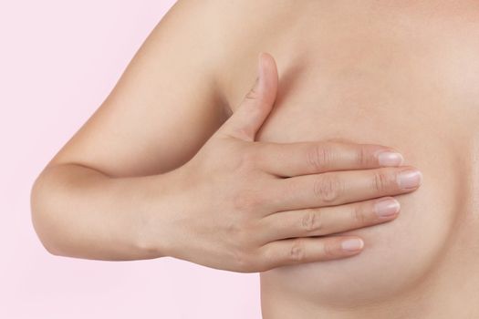 Breast cancer. Female hand touching naked breast isolated on pink background. Feminine health concept.