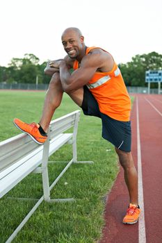 African American man in his 30s stretching out before a run at a sports track outdoors.