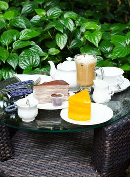 Coffee, tea, chocolate crape cake and orange cake on table in garden