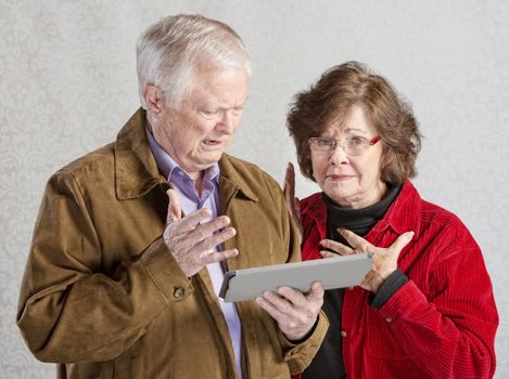 Overwhelmed senior man and woman holding tablet