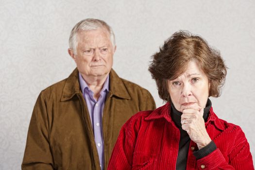 Serious woman with hand on chin with man watching