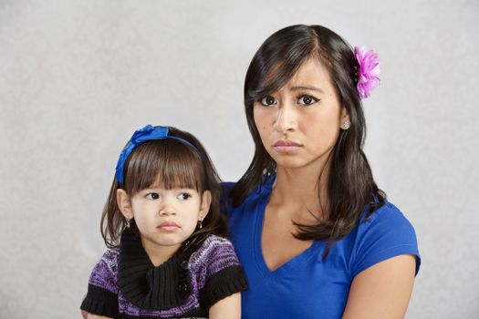 Disappointed Asian mother holding serious female toddler