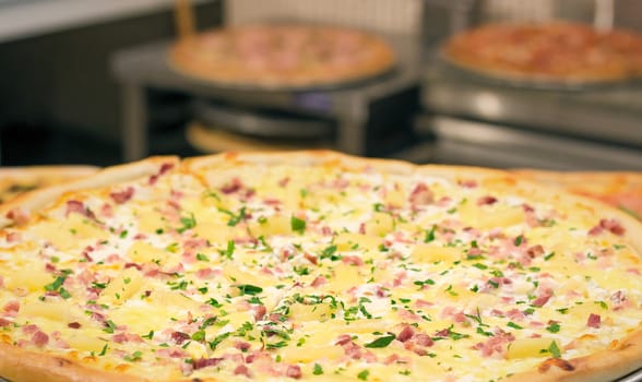 Big pizza on a dish with ham, cheese, the parsley greens, prepared at restaurant.