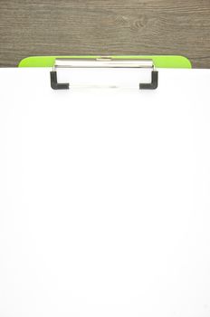 Write blank paper clip on green clipboard with wood background.