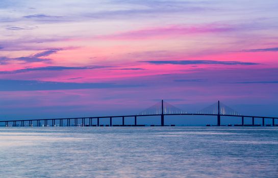 Panorama of bright sunrise lighting up the sky behind Sunshine Skyway Bridge from St Petersburg Florida across Tampa Bay.