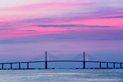 Brilliant sunrise lights up the sky behind Sunshine Skyway Bridge from St Petersburg Florida across Tampa Bay.