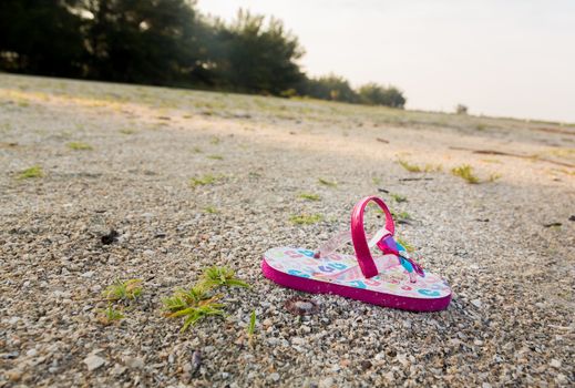 Concept image of the threat for child kidnapping or Amber alert with a single toddlers sandal alone on large beach with no sign of anyone
