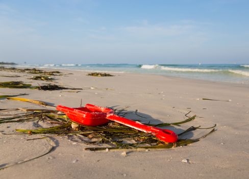Lost or abandoned red childs spade on sandy beach with ocean in distance to give concept of loss or danger