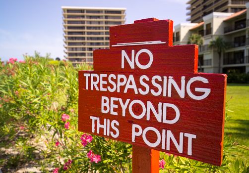 Large no trespassing sign in front of flower gardens in holiday resort or private apartments by beach in Florida