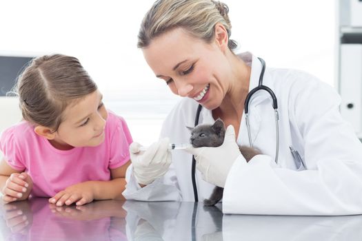 Female vet giving cat medicine through mouth with girl in clinic