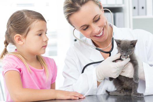 Happy female veterinarian examining kitten with girl in clinic