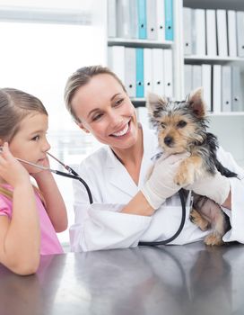 Female vet with little girl examining puppy in clinic