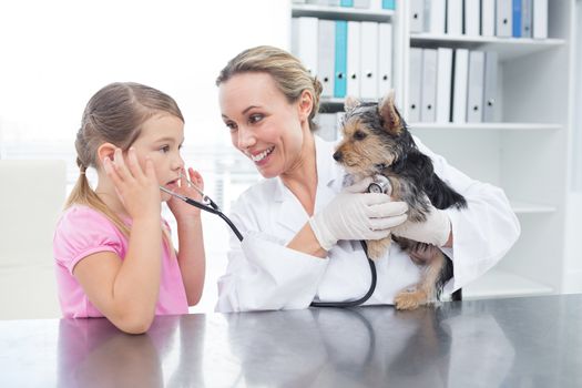 Female vet with girl examining puppy in clinic
