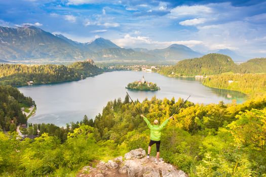 Made it. Young spoty active lady with hiking sticks and hands rised admiring beautiful nature around Bled Lake in Julian Alps, Slovenia. 
