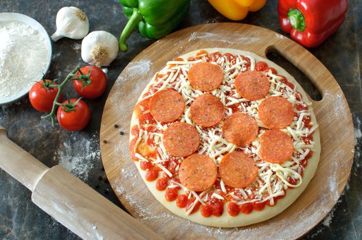Pepperoni pizza preparation with rolling pin and fresh ingredients on the side