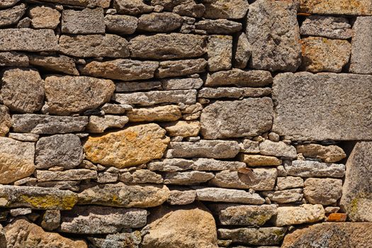 Textured wall surface in a small village of Spain made from granite and a  bird captured flying at the right bottom side of the picture