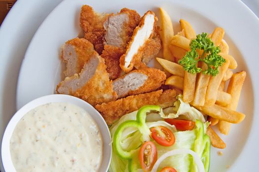 Plated lunch of chicken strips, french fries with ketchup and dipping sauce.