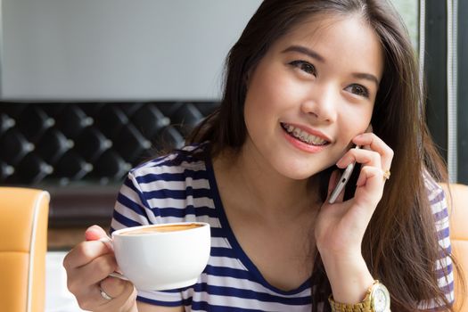 Beautiful woman talking on the phone and  holding cup of coffee at cafe
