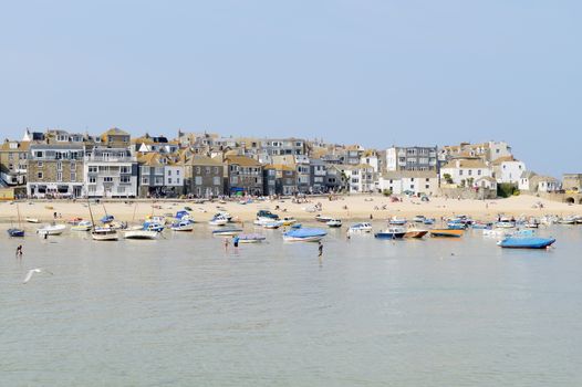 Sunny cornish beach in the summer with boats moored in the harbour