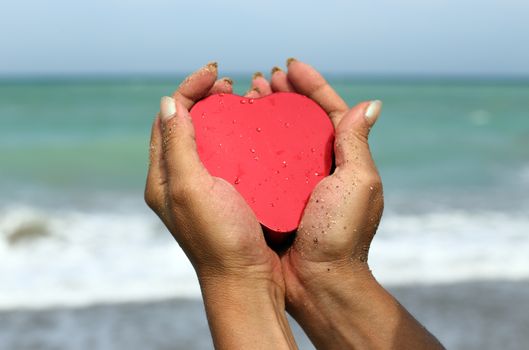 Woman  hands holding a red heart shape at the beach horizontal picture