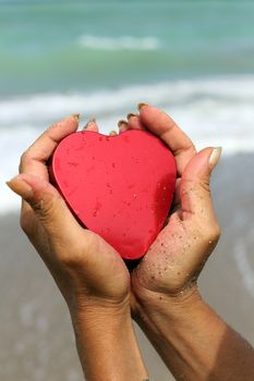 Woman  hands holding a red heart shape at the beach vertical picture