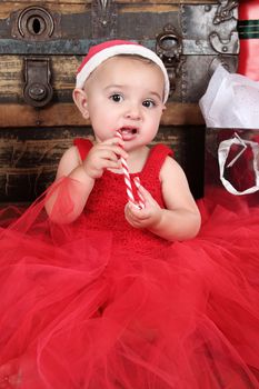 Brunette baby girl wearing a red christmas dress eating candy