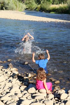 Three kids playing in shallow water on pebble beach