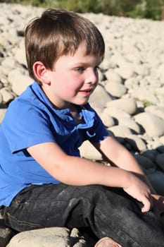 Younb boy sitting outside on pebble beach