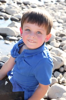 Younb boy sitting outside on pebble beach